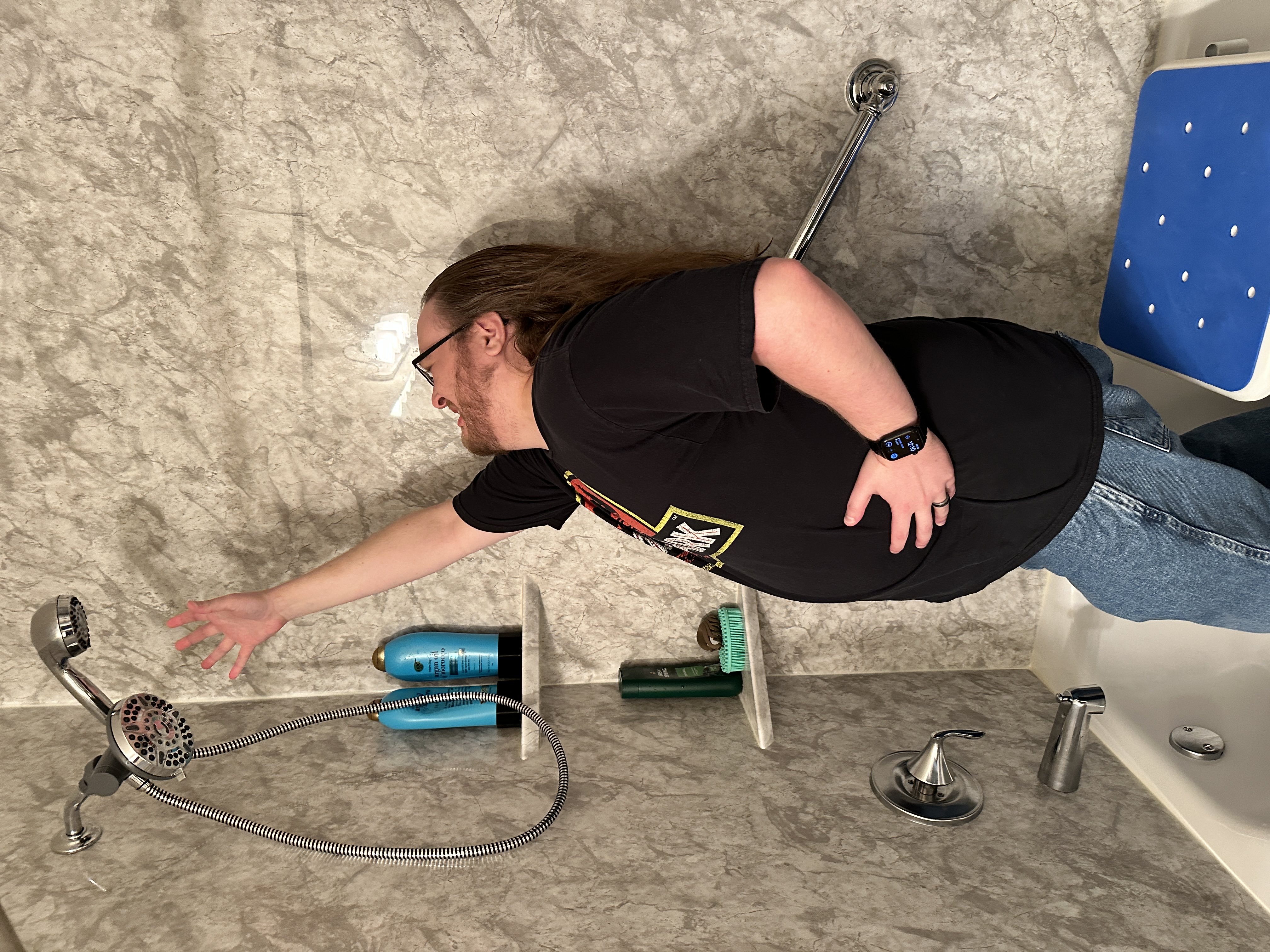 The article author, Tom, standing in a shower, fully clothed. He is reaching
towards a shower head that has a separate wand attachment near the main faucet
head. He has an exaggerated pain expression as he reaches for the wand
ineffectually. An accessible waterproof shower seat is to his right. This image
humorously illustrates the pain he would have to endure if he wanted to reach
the shower
wand.