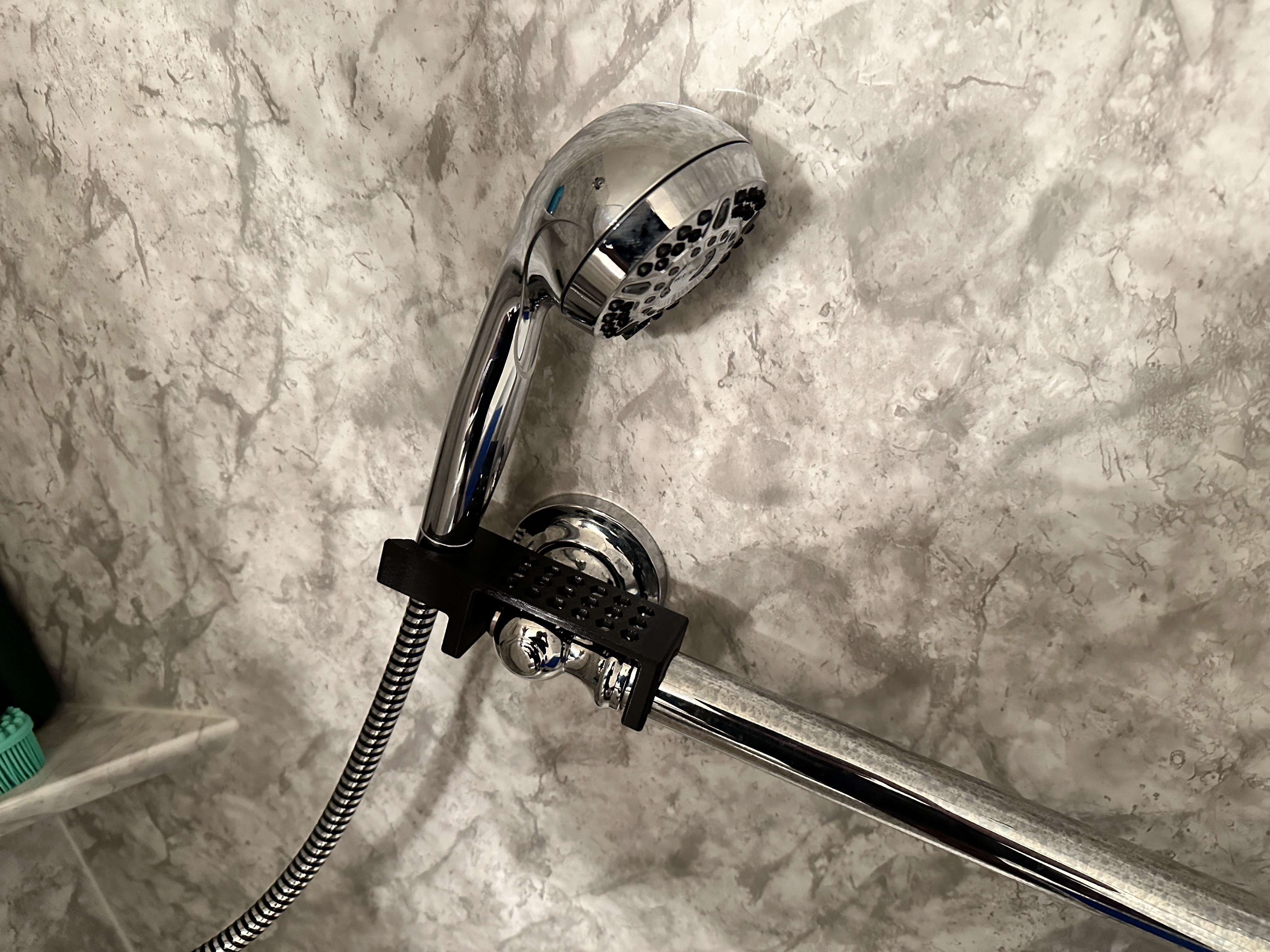 The 3D printed shower wand grab bar mount part mounted on a shower grab bar. This image shows the part in actual use with the shower wand resting in the part, being held securely.